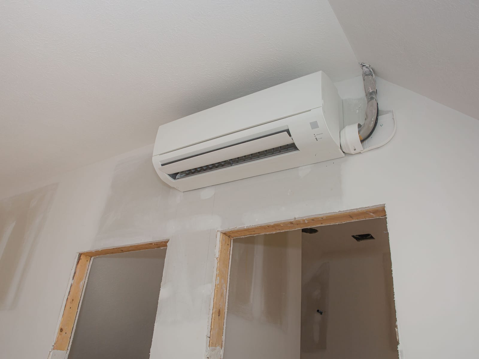 Ductless mini-split head installed high on a wall in a home under construction with framed openings below