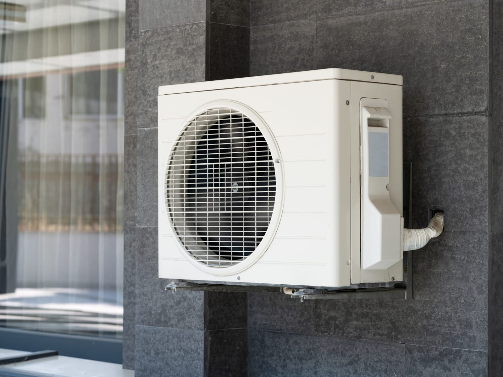 Outdoor heat pump condenser unit bracket-mounted on an exterior wall with insulated refrigerant lines