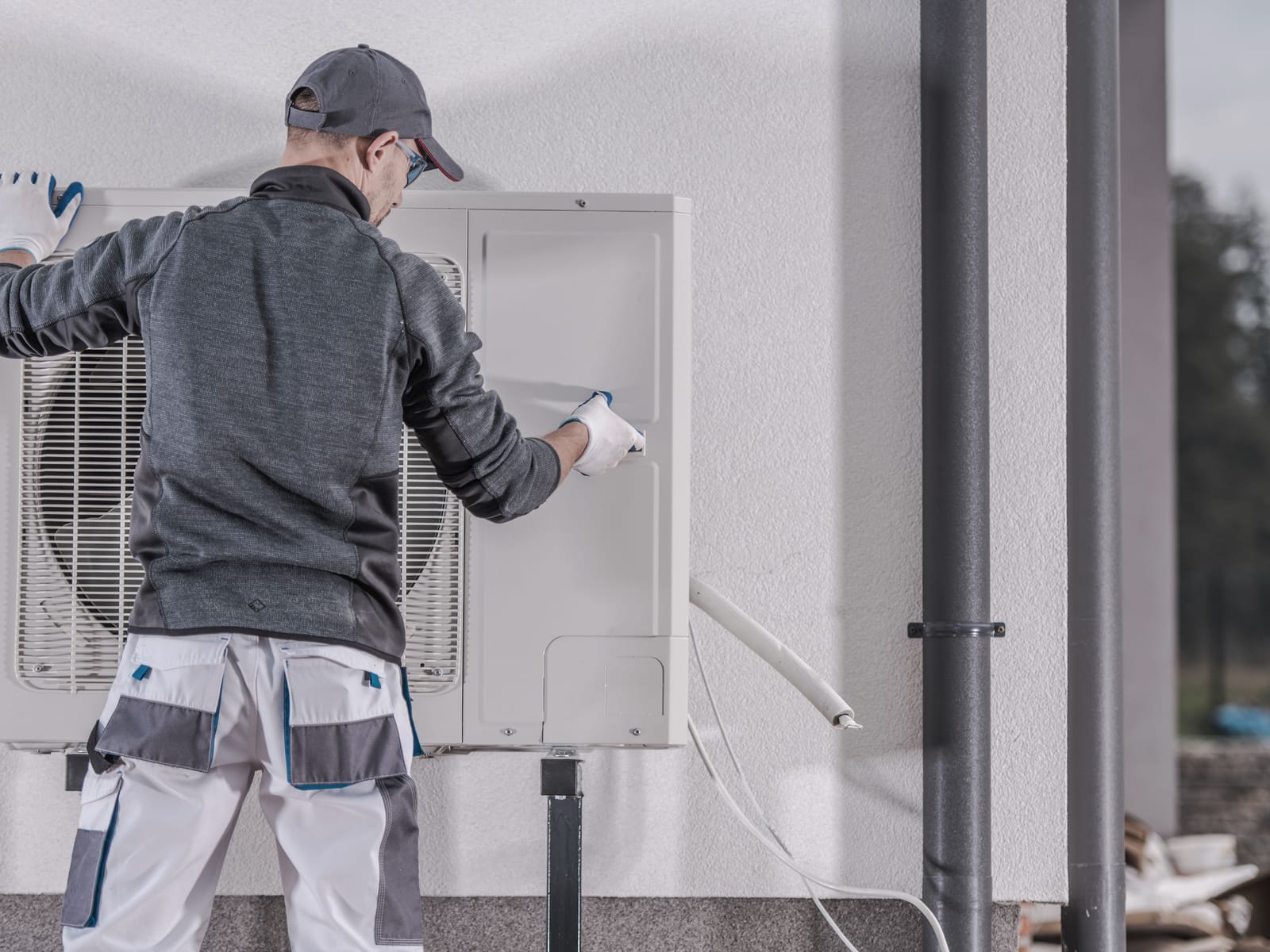 Rytek Construction technician servicing an outdoor heat pump unit mounted beside a home