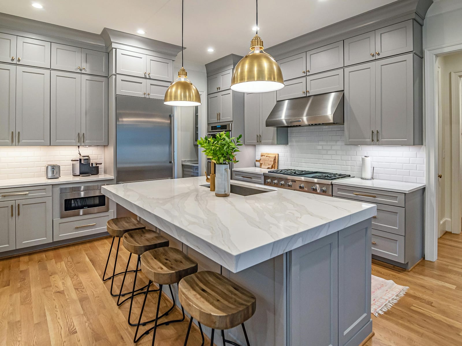 Renovated kitchen with grey shaker cabinetry, a marble-topped island, brass pendant lighting and hardwood flooring