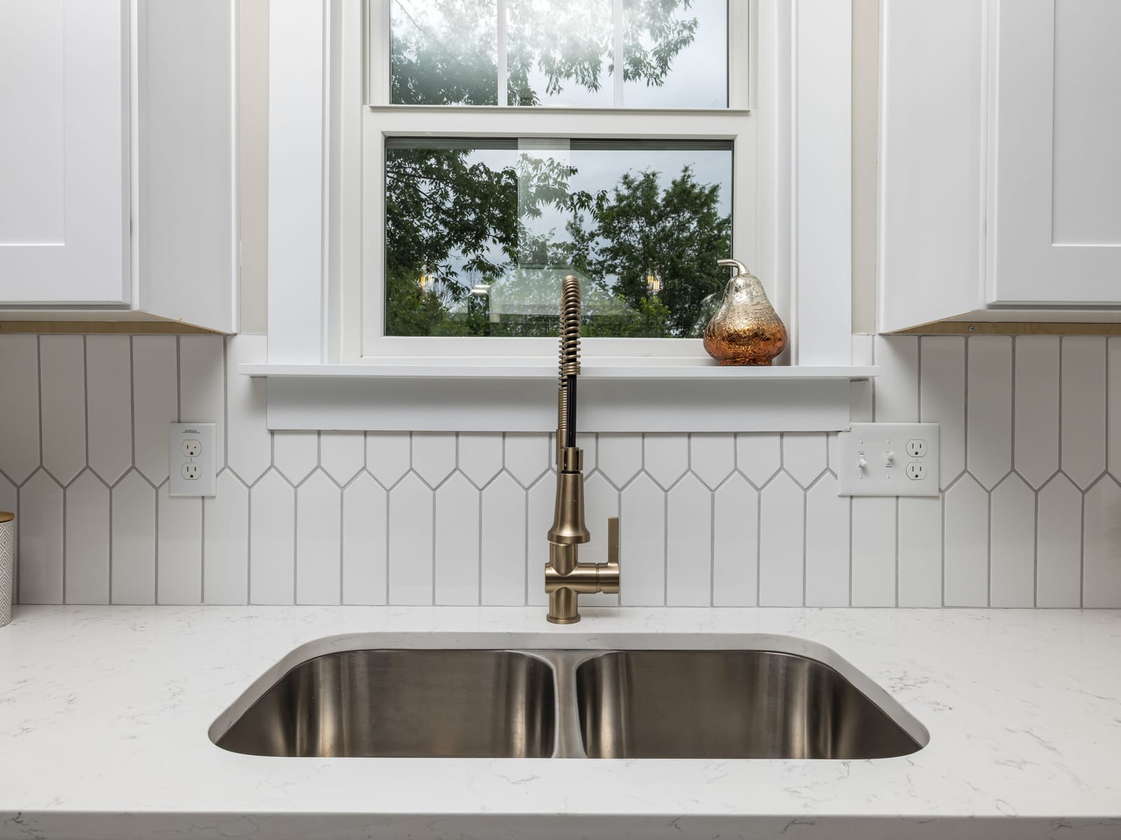 Undermount stainless kitchen sink with a brass pull-down faucet set in a quartz countertop