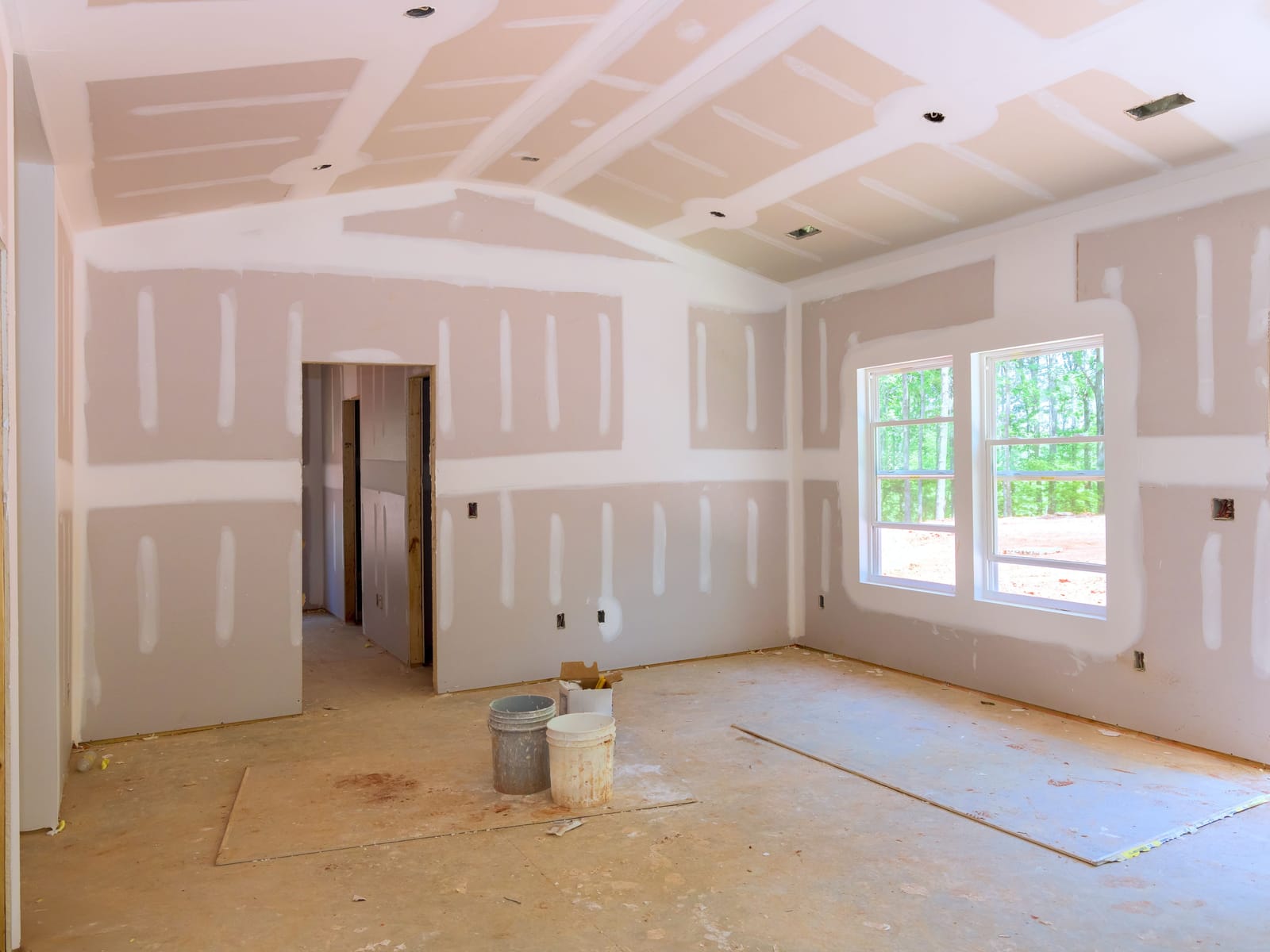 Interior of a new home with taped and mudded drywall, a vaulted ceiling, and newly installed windows