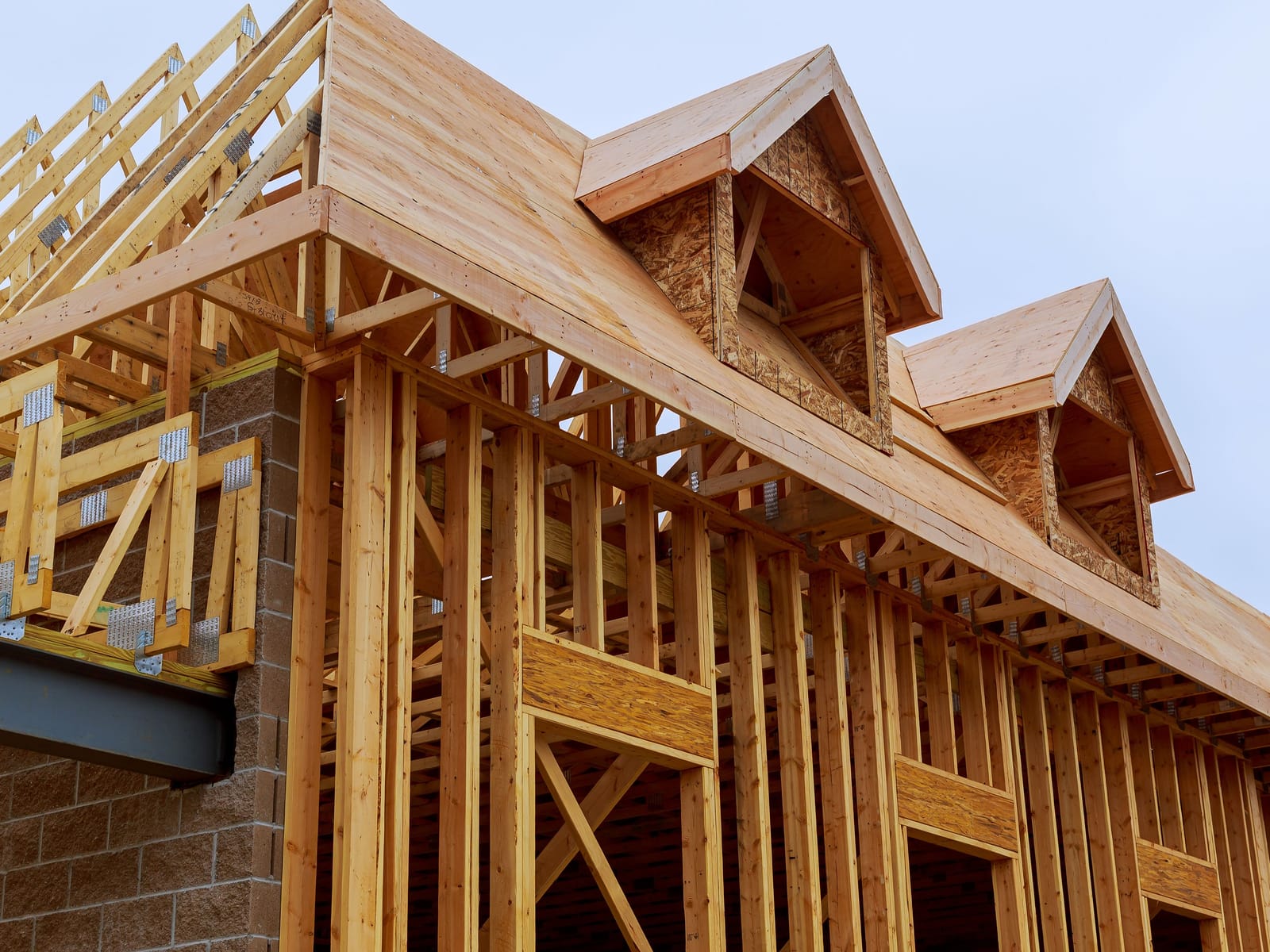 Roof framing on a new home under construction, with dormers and engineered trusses against a clear sky