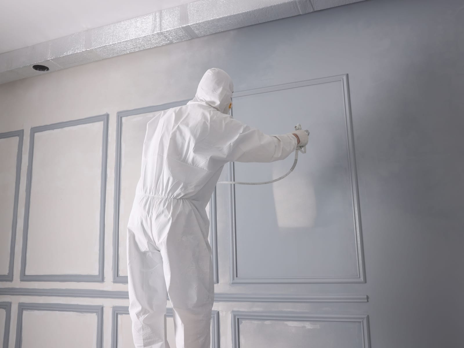 Painter in protective coveralls spray-painting wall panelling with a fine, even finish
