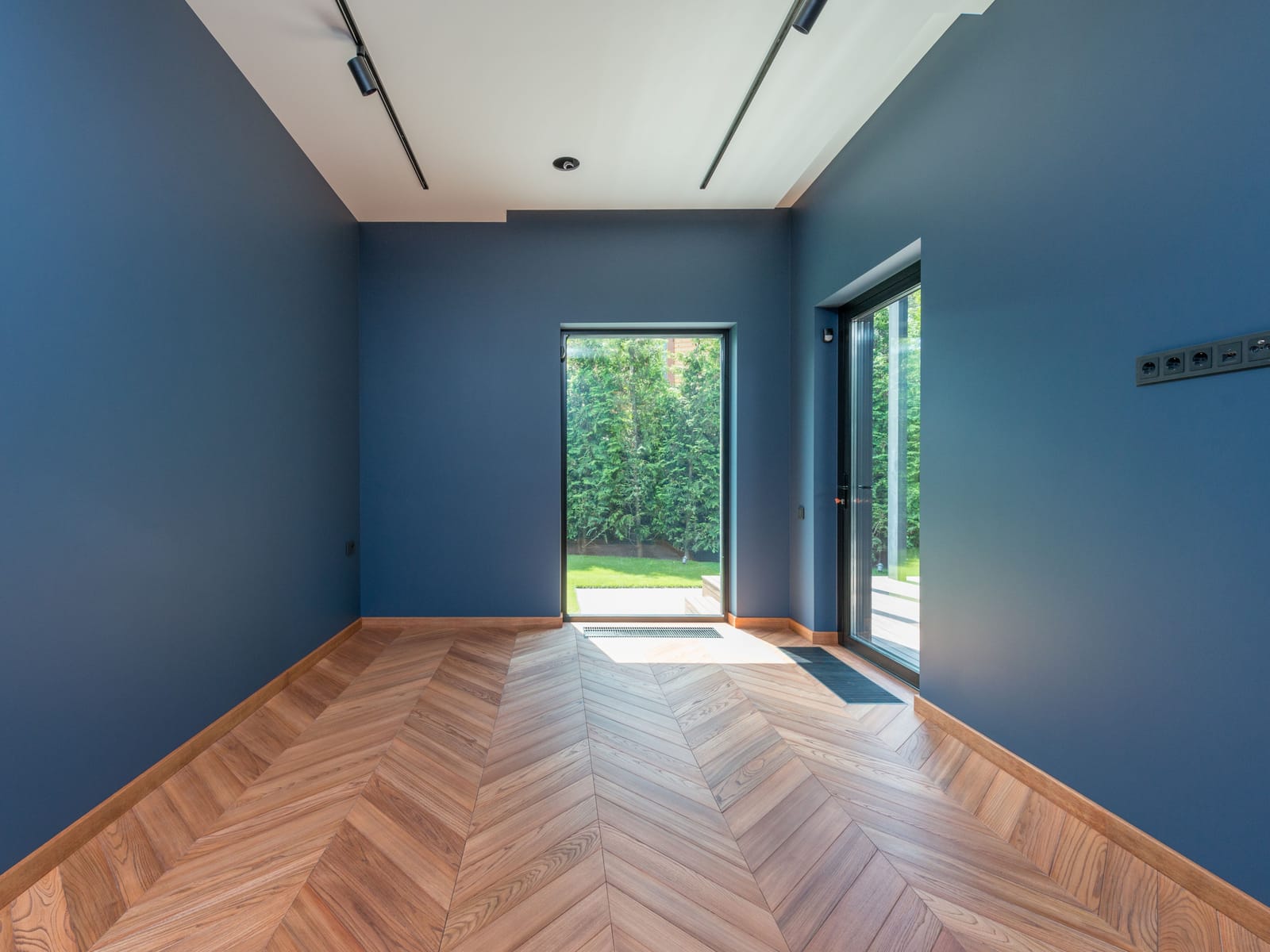 Finished room painted in a deep blue with a crisp white ceiling and chevron hardwood flooring