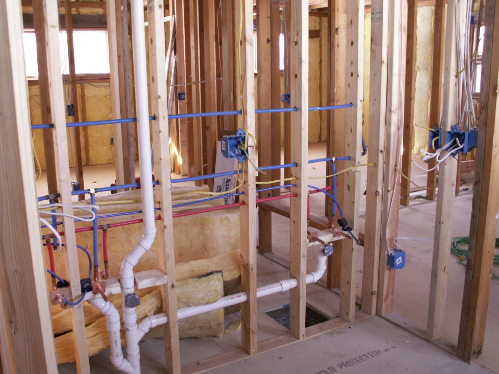 Hot and cold water lines and PVC drain piping roughed in through open wall framing before drywall