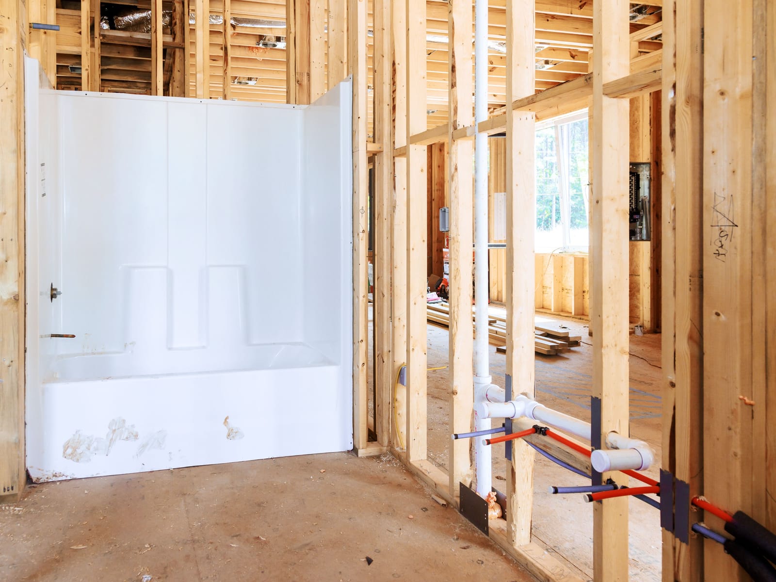 Bathtub and shower surround set in place with water and drain lines roughed in through the framing